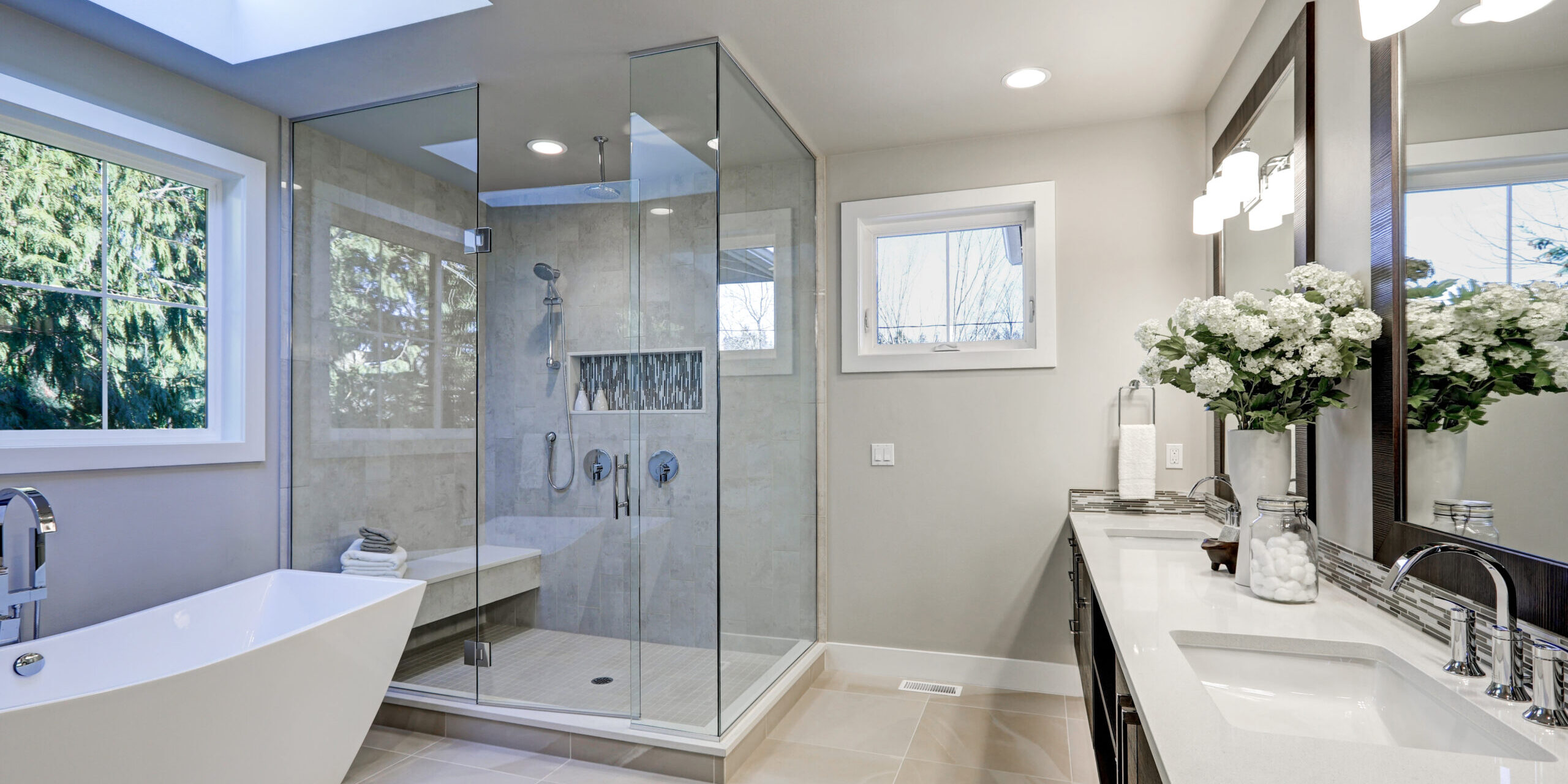 Spacious bathroom in gray tones with heated floors, freestanding tub, walk-in shower, double sink vanity and skylights. Northwest, USA