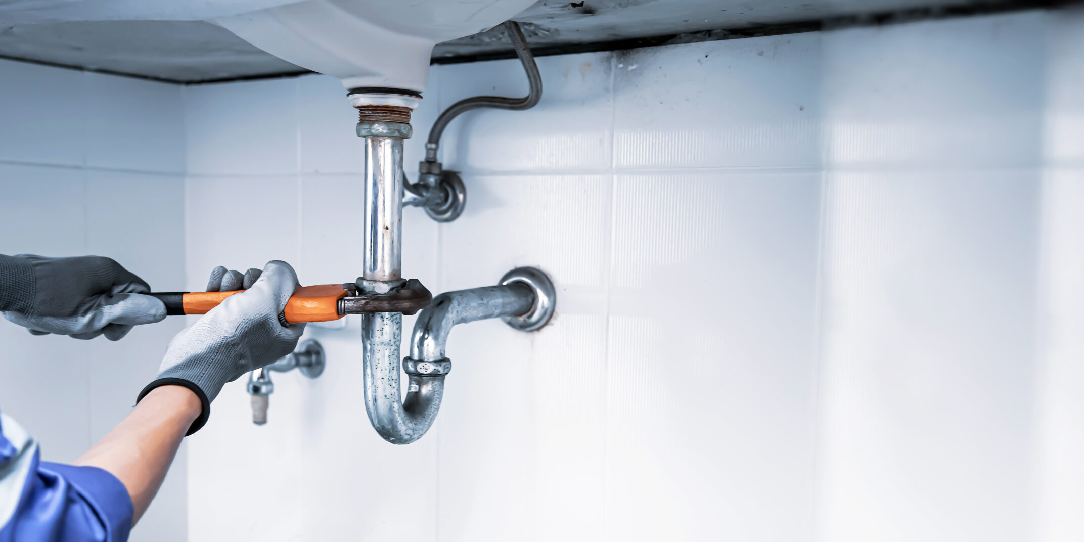 Technician plumber using a wrench to repair a water pipe under the sink. Concept of maintenance, fix water plumbing leaks, replace the kitchen sink drain, cleaning clogged pipes is dirty or rusty.